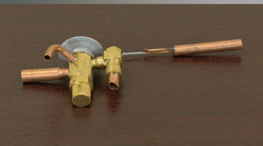 The device has copper tubing connections for refrigerant flow and a metal capillary tube connected to a bulb, used to regulate the refrigerant flow in HVAC systems by controlling superheat. The item ensures efficient cooling by adjusting the refrigerant entering the evaporator coil based on system load.