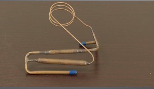 A coiled copper capillary tube with two cylindrical sections, used as a component in HVAC systems for precise refrigerant flow control. The device is designed to regulate the flow of refrigerant by reducing pressure, ensuring efficient cooling.