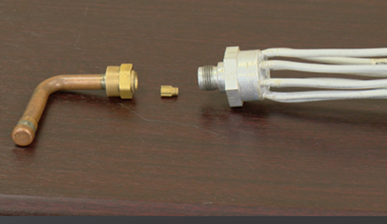 On the left is an L-shaped copper tube with a brass fitting, in the center is a small brass flow control element, and on the right is a larger fitting with multiple white tubes extending from it. This device is typically used in HVAC systems to regulate the flow of refrigerant.