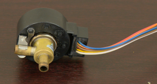 The valve consists of a brass body with a cylindrical black housing, which contains the electronic control components. Multi-colored wires (blue, orange, white, and brown) are attached to the right side of the black housing, indicating the electrical connection used to control the valve's operation. The valve controls the flow of refrigerant in HVAC systems for precise temperature regulation.