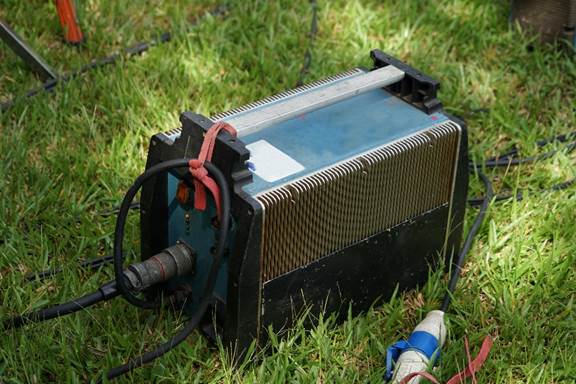 Large heavy rectangular box with handle on the top. Features a power switch, status lights, and has a thick cord plugged into it. Used for converting electrical power for lighting equipment.